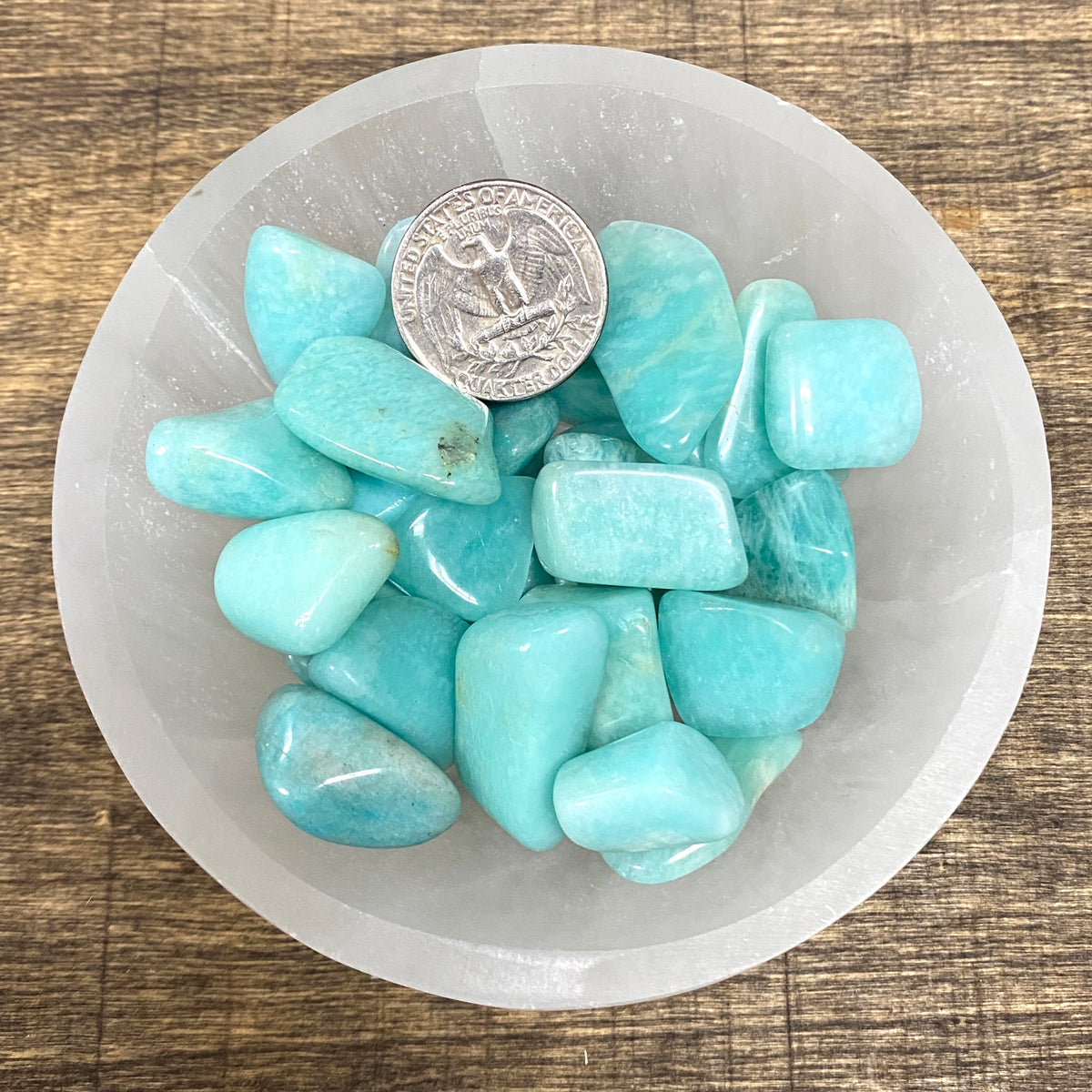 Overhead comparison shot of a US quarter coin and various Amazonite tumbled stones in a small bowl.