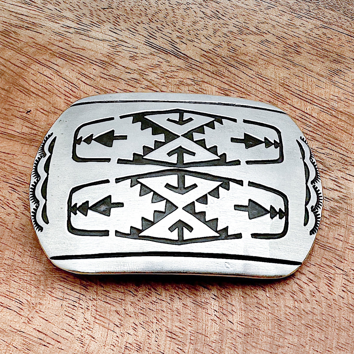 A sterling silver belt buckle with etchings of rain clouds and arrows on the front