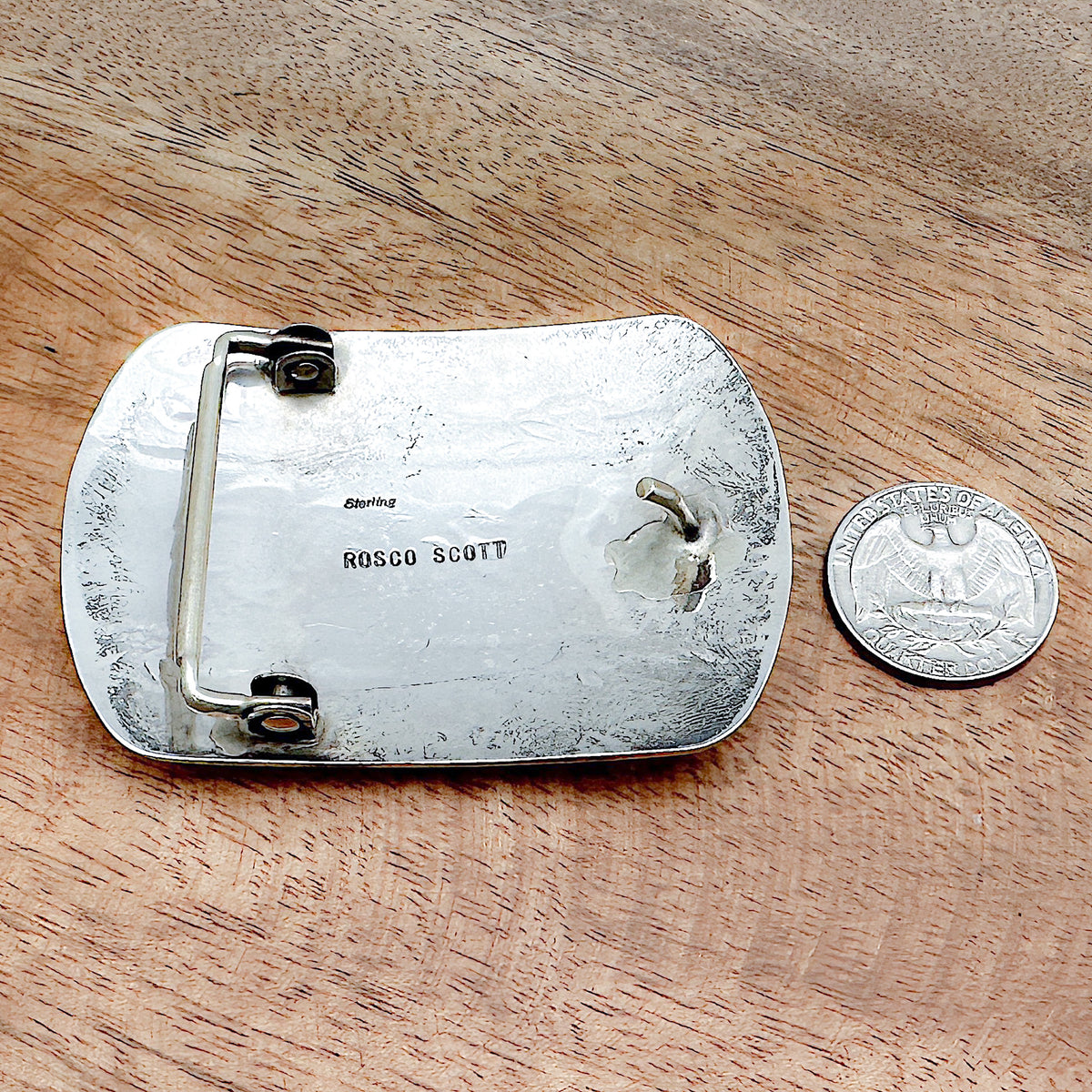Comparison shot of backside of silver bear paw belt buckle and a US quarter coin