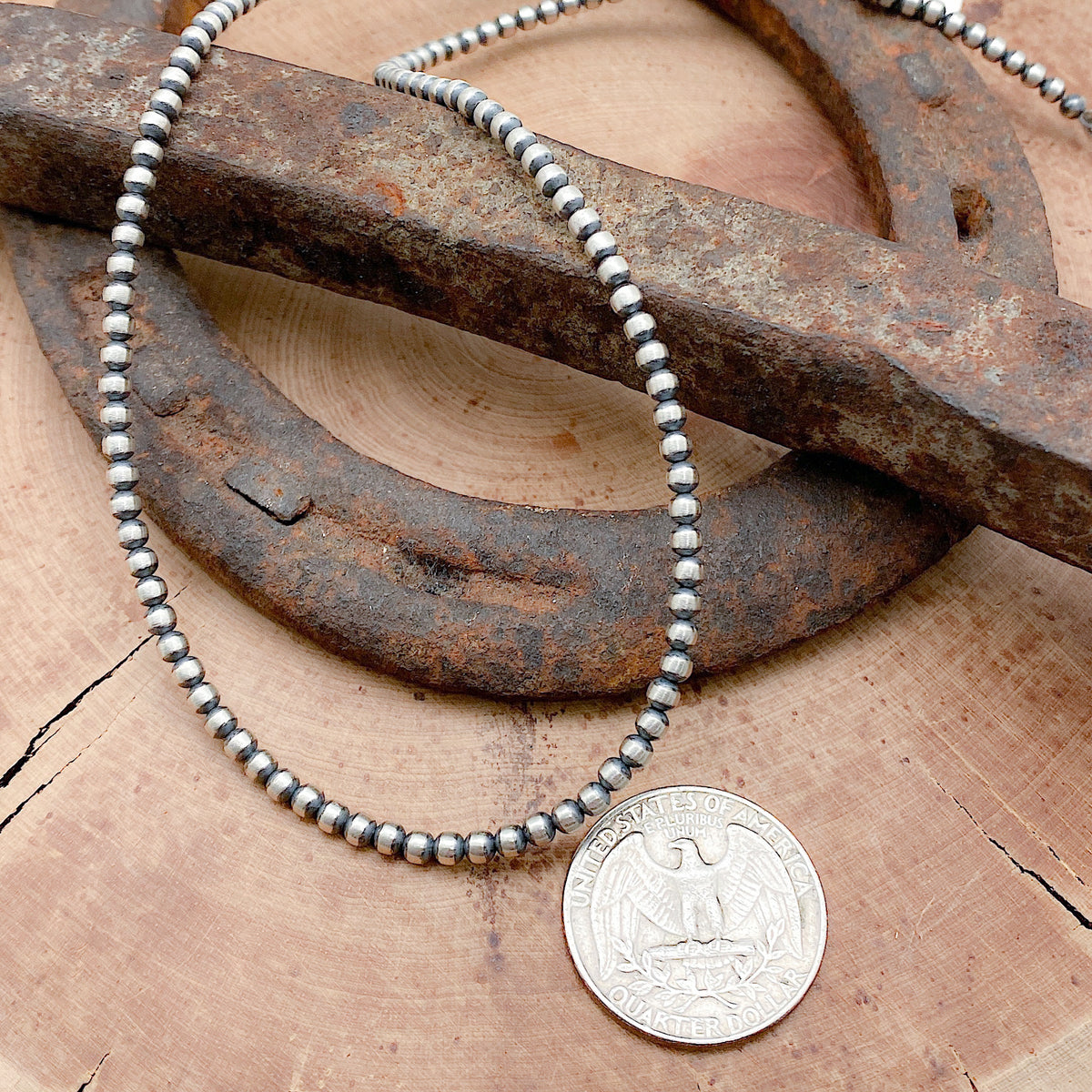 Size comparison of a US Quarter coin and a sterling silver hand crafted necklace that features 3mm beads an antiqued finish, and has a hook and eye clasp