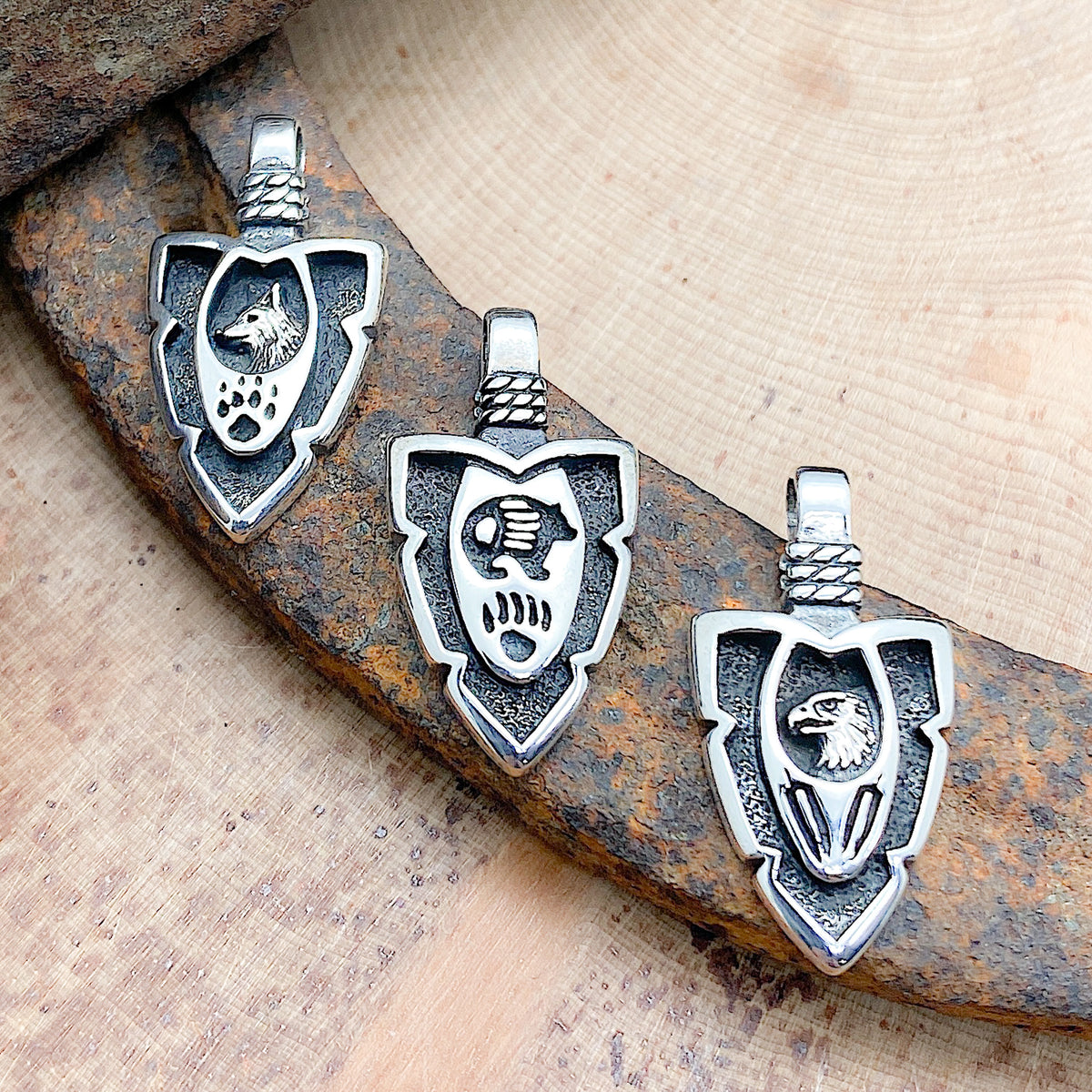 Various arrowhead pendants laid in a row, each with a different animal and symbol etched within the pendant.