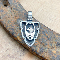 An arrowhead pendant with a wolf head and paw etched into the pendant