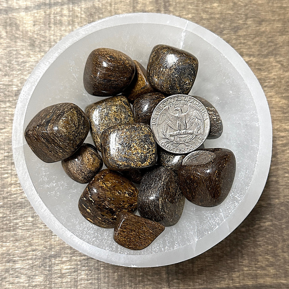 Comparison shot of a US quarter coin and various bronzite tumbled stones in a bowl