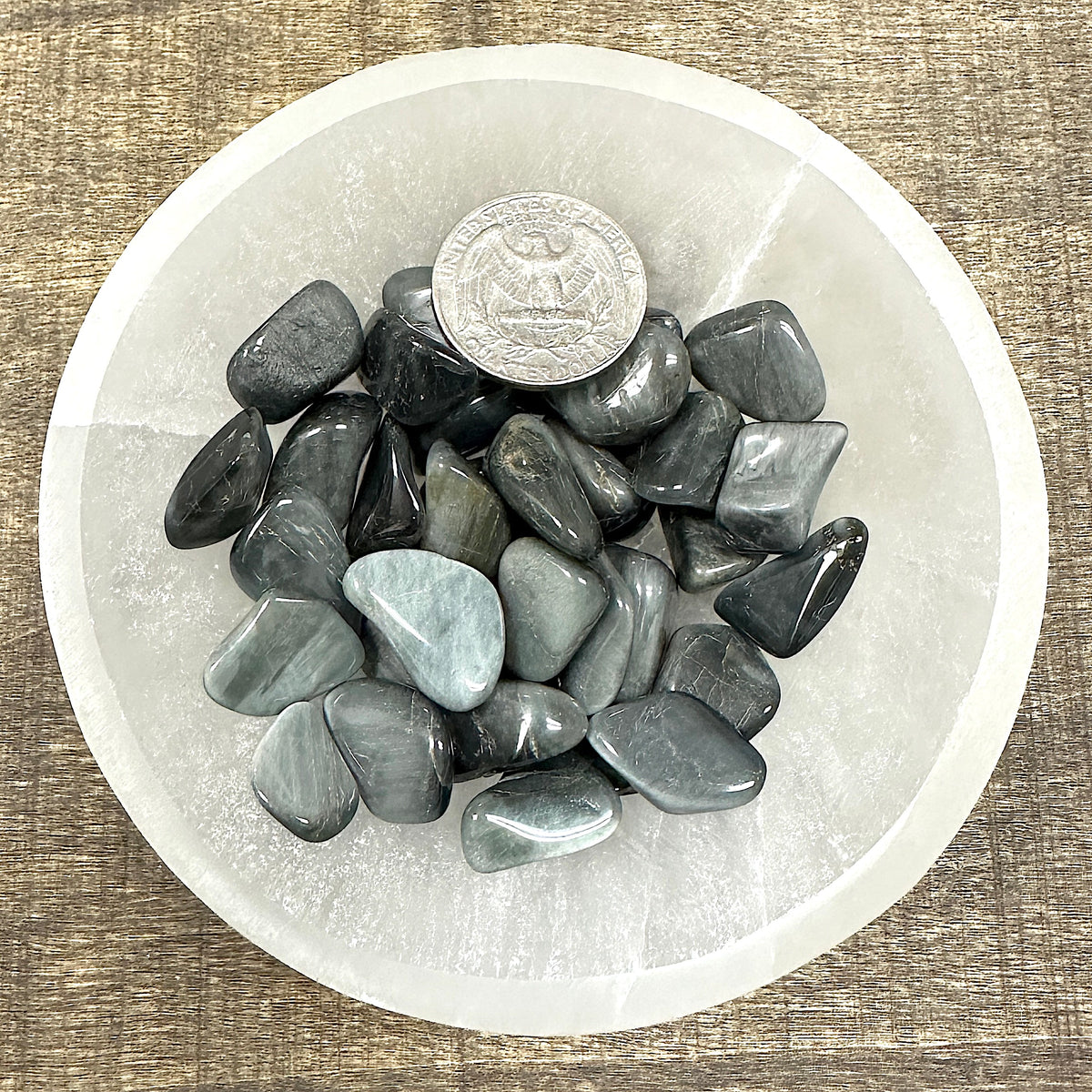 Comparison shot of a US quarter coin and various Cat's Eye tumbled stones in a bowl