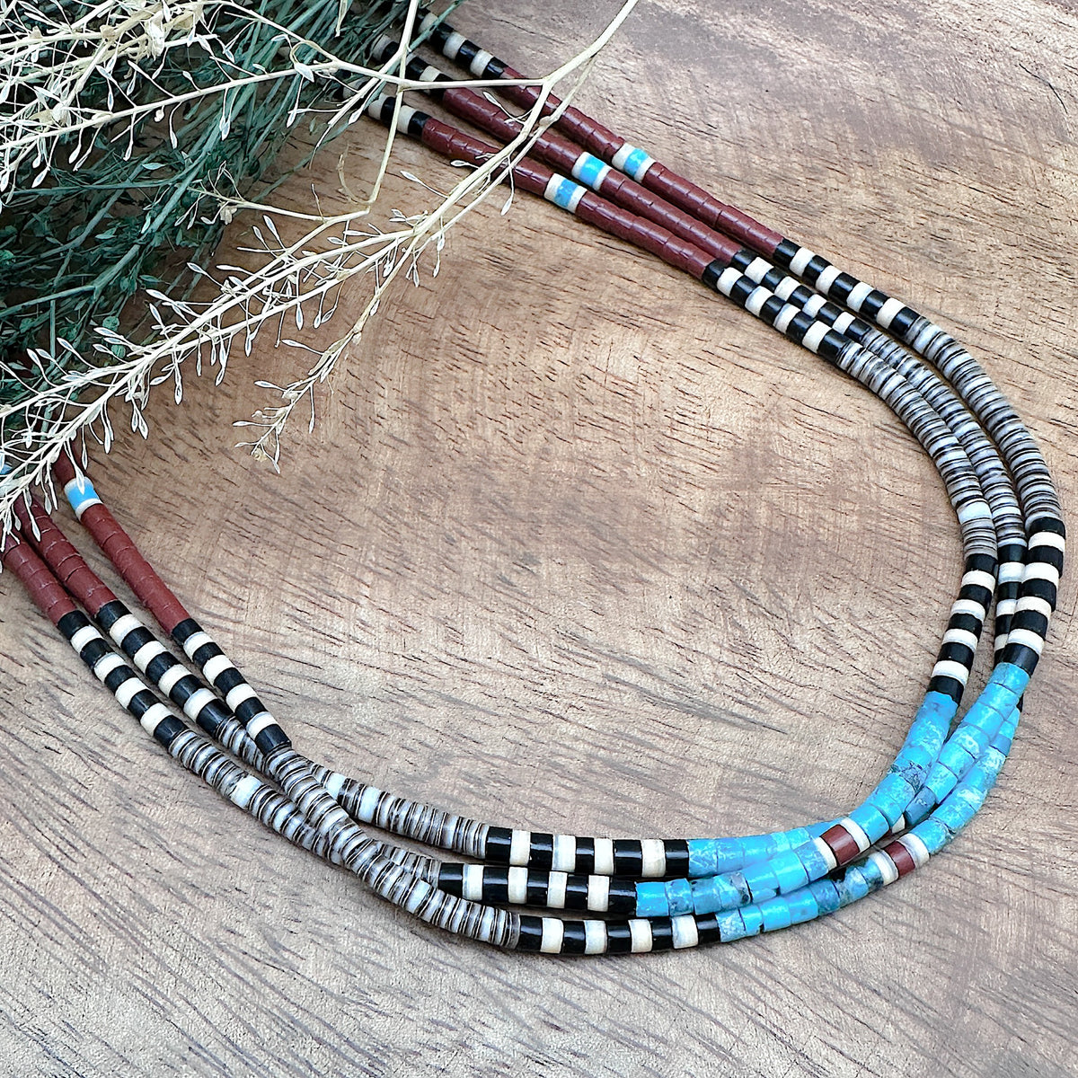 A handmade three strand Heishi necklace that features a variety of stones and shells with sterling silver findings.