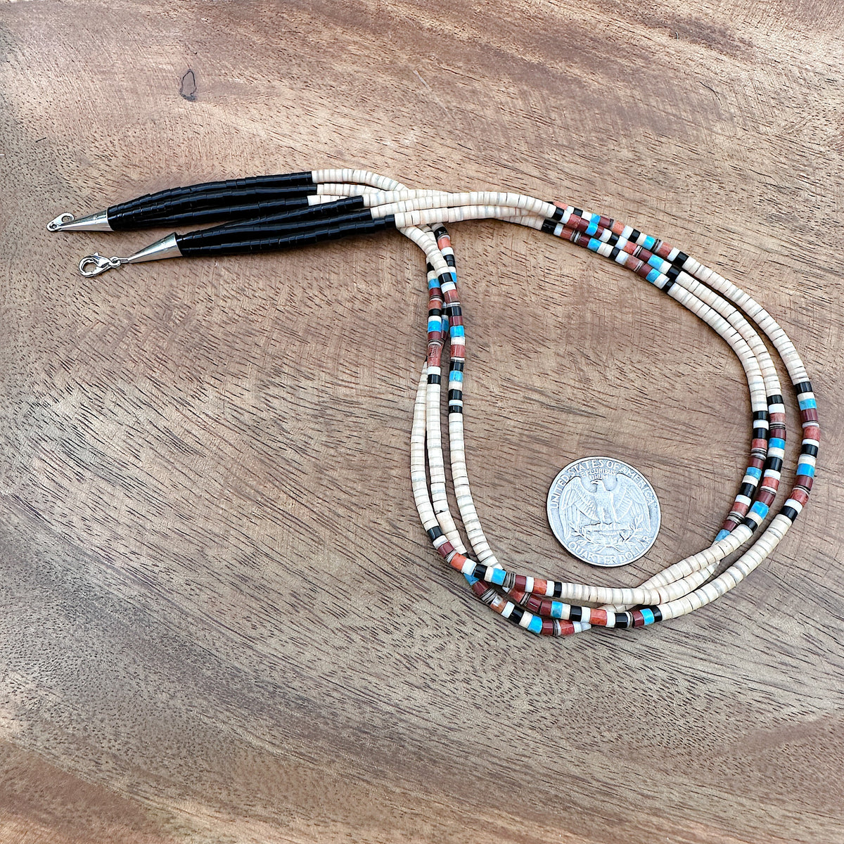 Size comparison of a US quarter coin and a handmade three strand Heishi necklace that features a variety of stones and shells with sterling silver findings.