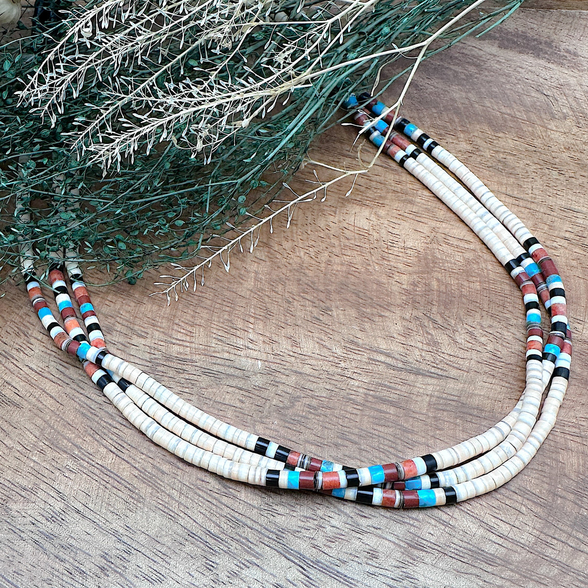 A handmade three strand Heishi necklace that features a variety of stones and shells with sterling silver findings.