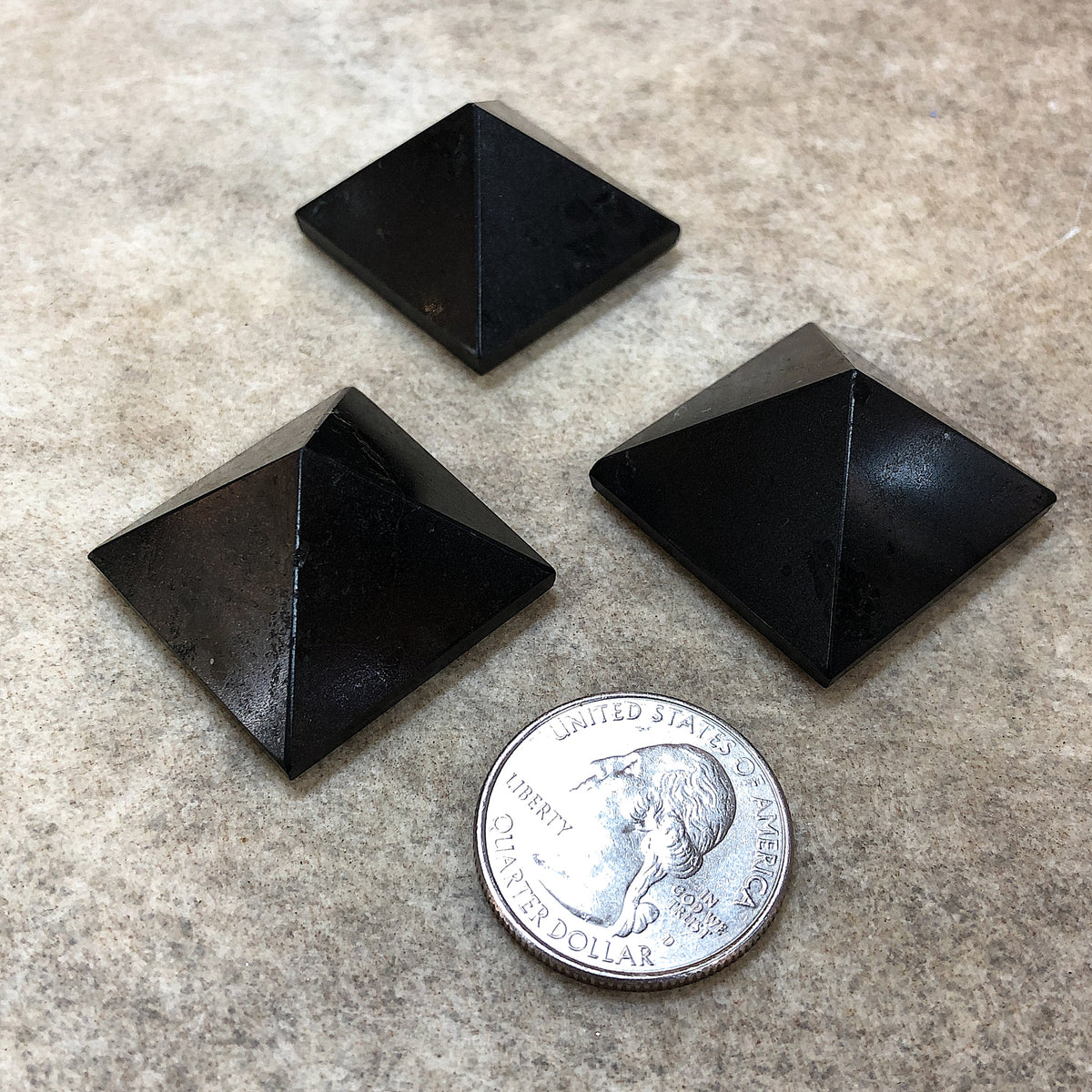 Comparison shot of three black tourmaline pyramids and a US quarter coin