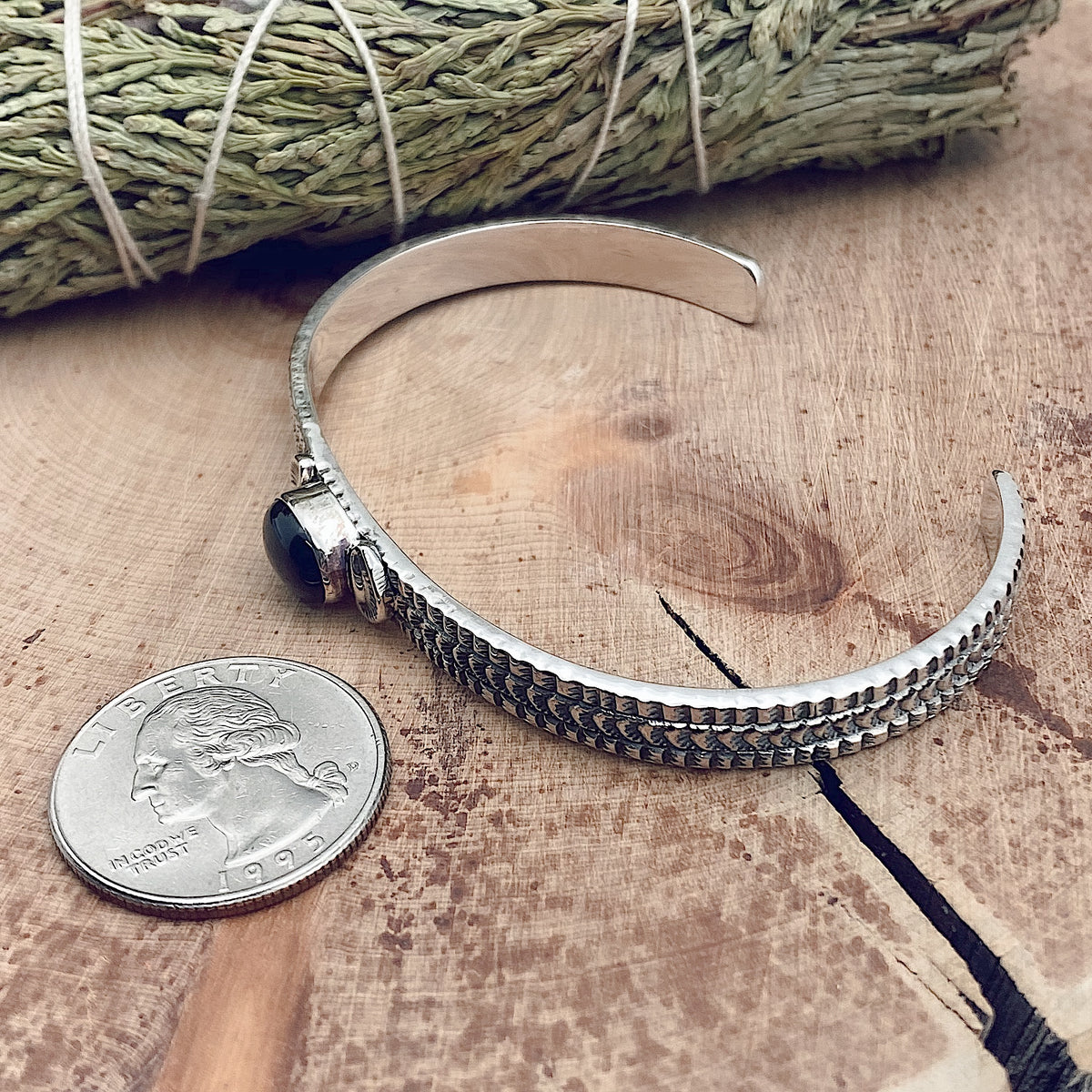 Comparison shot of a US quarter coin and a black onyx stamped cuff bracelet as viewed from the side