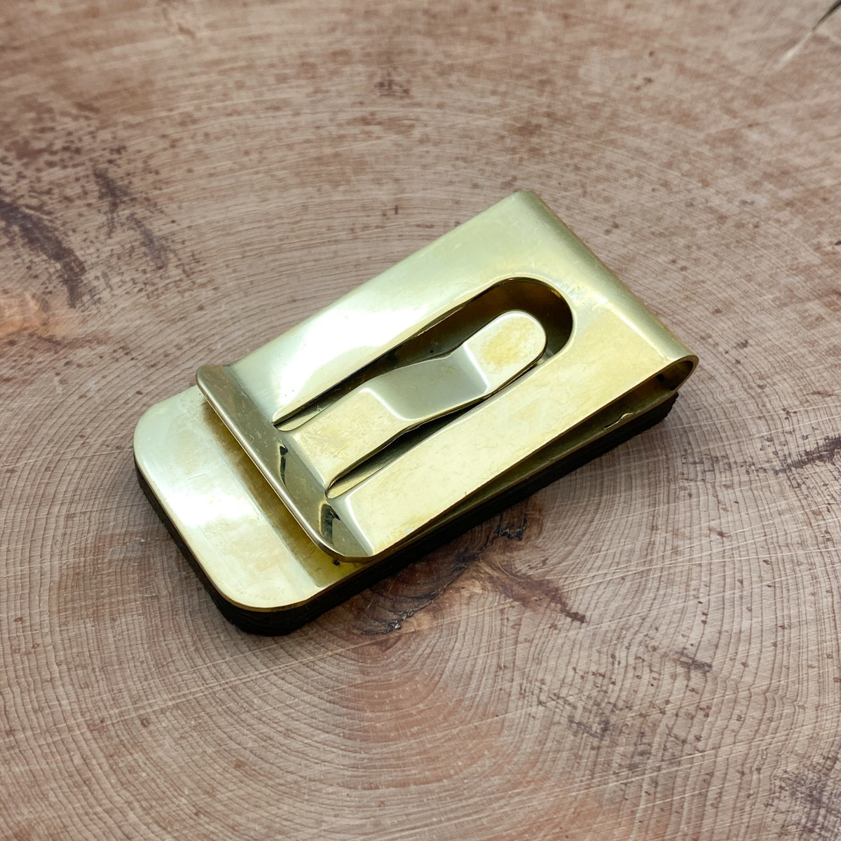 The brass backside of an authentic 1904 Chief Penny money clip that is set into natural wood.