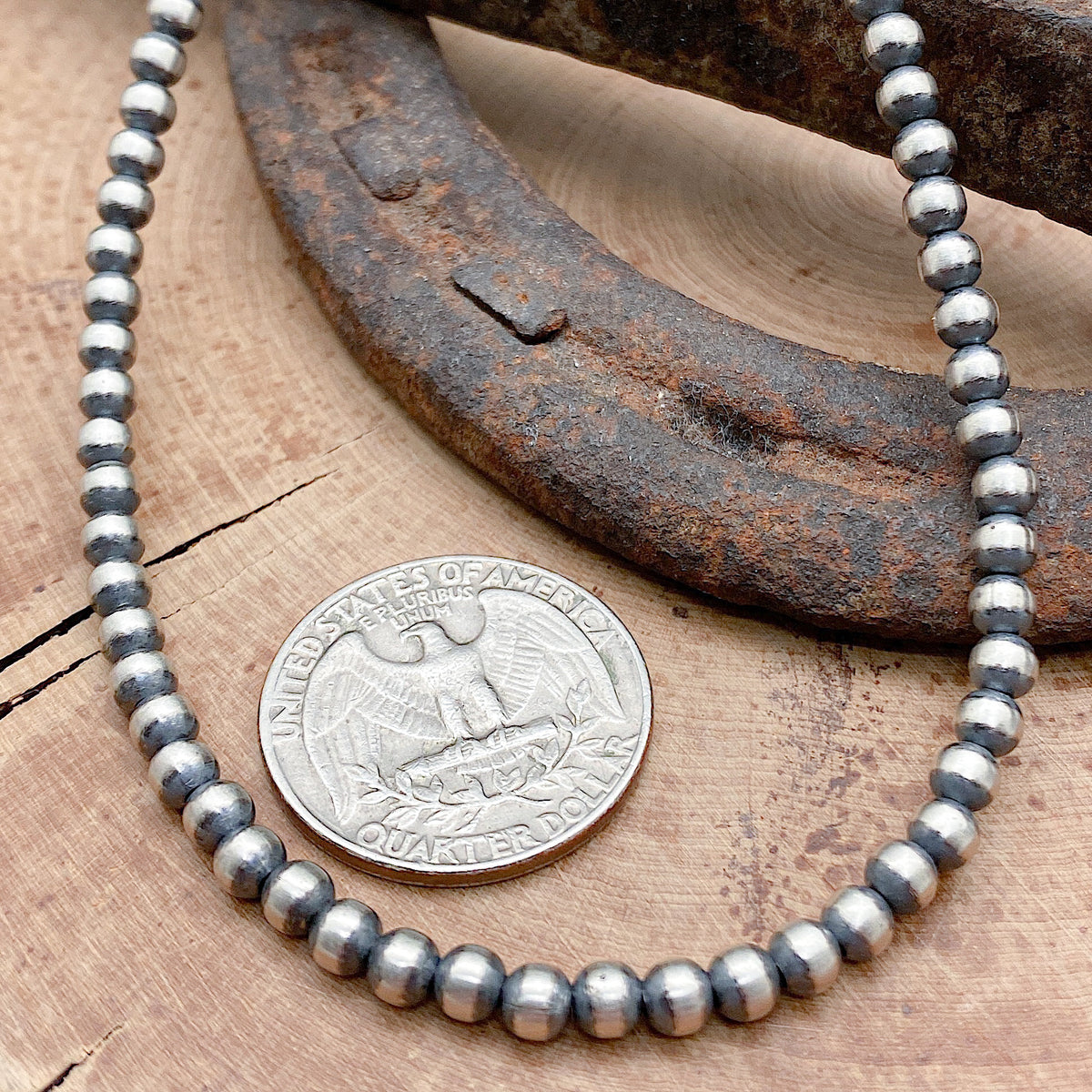 Size comparison between a US Quarter coin and a Sterling silver hand crafted necklace that features 3mm beads, an antiqued finish and has a hook and eye clasp.