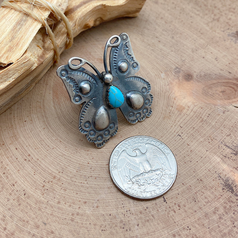 Comparison shot of a US quarter coin and a butterfly-shaped sterling silver ring with a teardrop-shaped turquoise stone embedded into the front