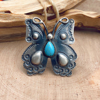 Shot of a sterling silver ring in the shape of an ornate butterfly with a teardrop-shaped turquoise stone embedded into the front of the ring