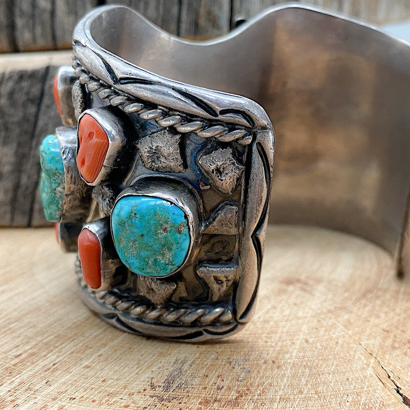 Side view of a large Native handmade sterling silver vintage watch cuff with natural sleeping beauty nugget turquoise and natural Mediterranean Red Coral set into the bracelet.
