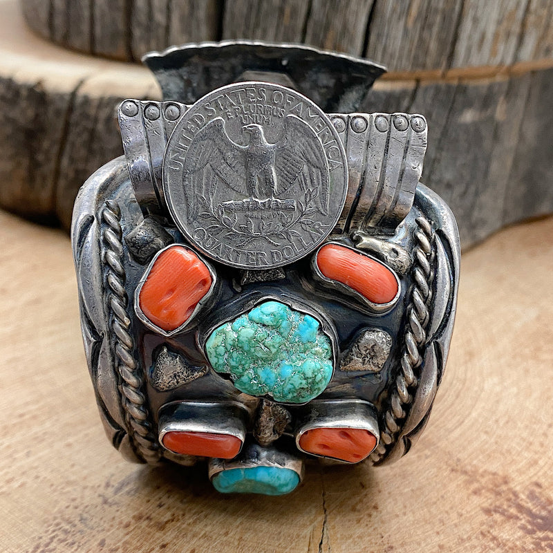 Size comparison of a US quarter coin in relation to a large Native handmade sterling silver vintage watch cuff with natural sleeping beauty nugget turquoise and natural Mediterranean Red Coral set into the bracelet.